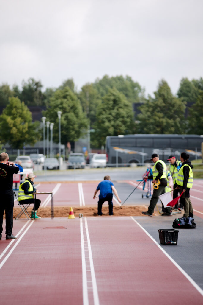 Osallistuja on hypännyt pituushypyn hiekalle. Toimitsijat mittaavat tulosta.