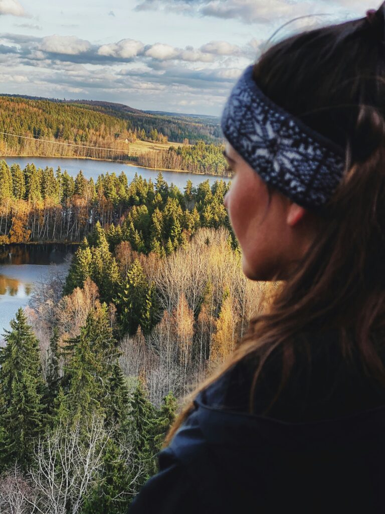 Nainen seisoo korkealla, taustalla näkyy metsää ja järviä