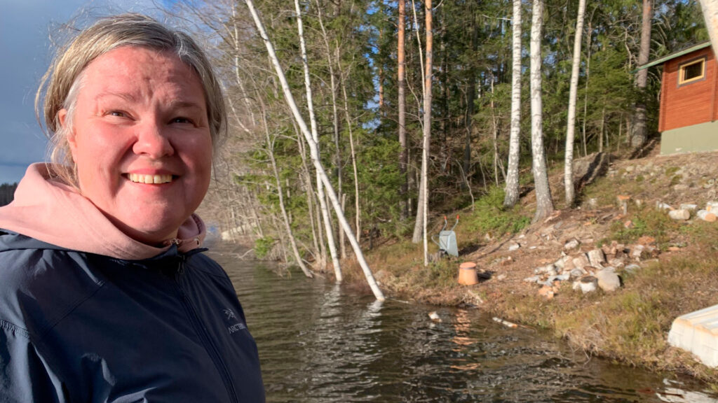 Paula Paloheimo hymyilee leveästi järven rannalla mökillään.