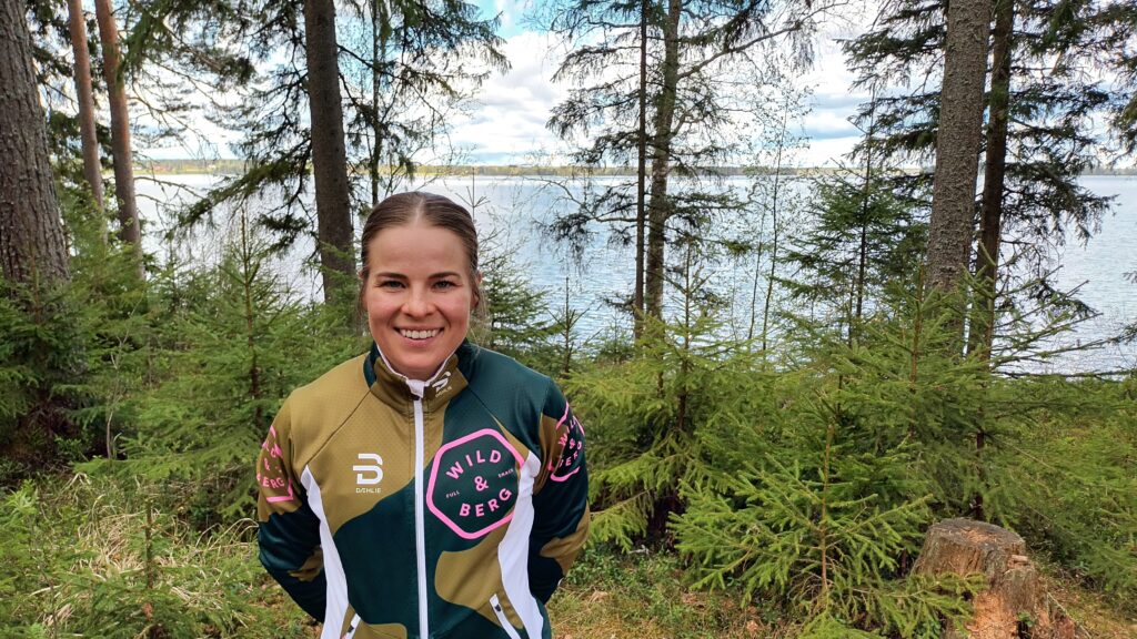 Krista Pärmäkoski hymyilee leveästi Kuortaneen järven rannalla metsässä.