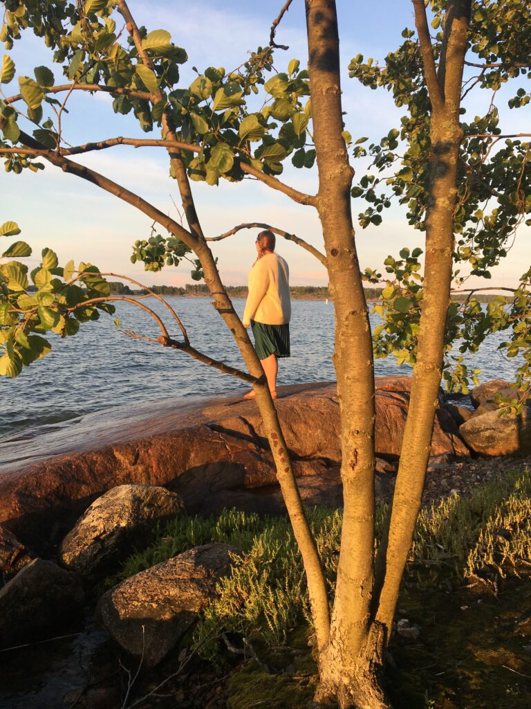 Nainen kävelee rantakalliolla auringon laskiessa merelle.