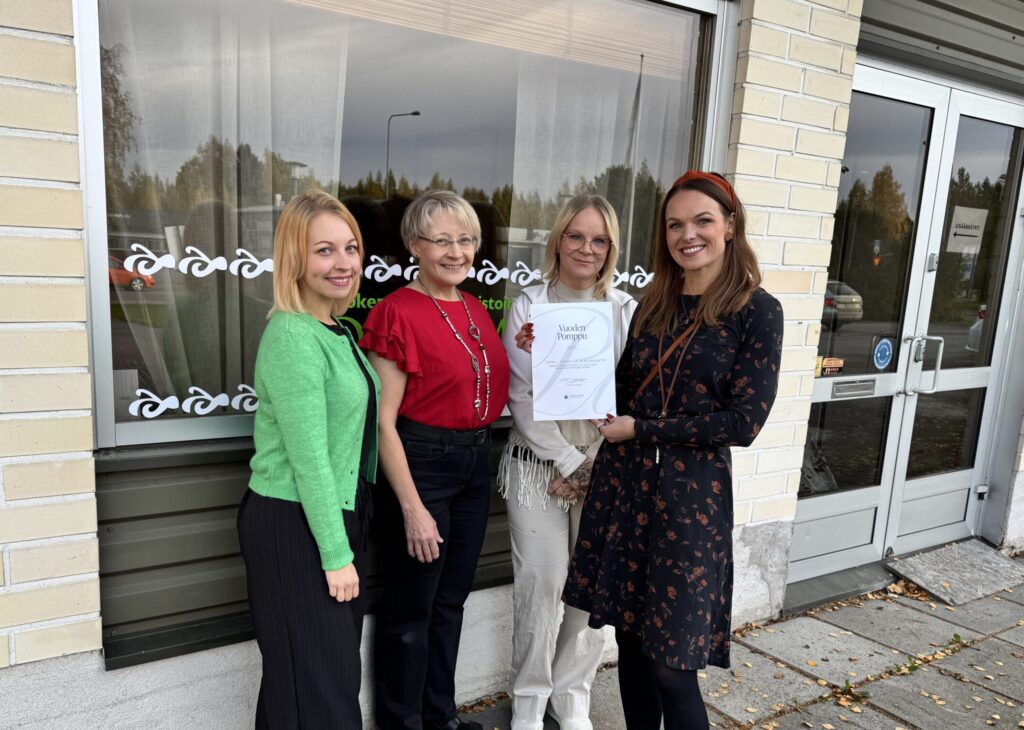 Olkkarin työntekijät hymyilevät kuvassa. Toiminnanjohtaja Sonja Orrenmaa pitää kädessään Vuoden Pomppu 2025 -kunniakirjaa.
