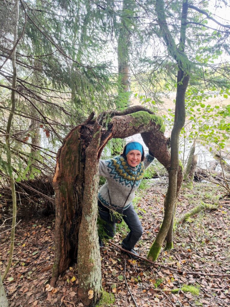 Susanne Blomqvist seisoo metsässä kaarelle taipuneen puunrungon alla.