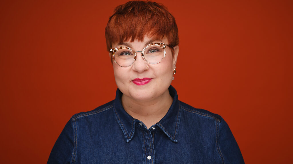 Emmi Nuorgam hymyilee. Hänellä on lyhyt punainen tukka ja silmälasit.