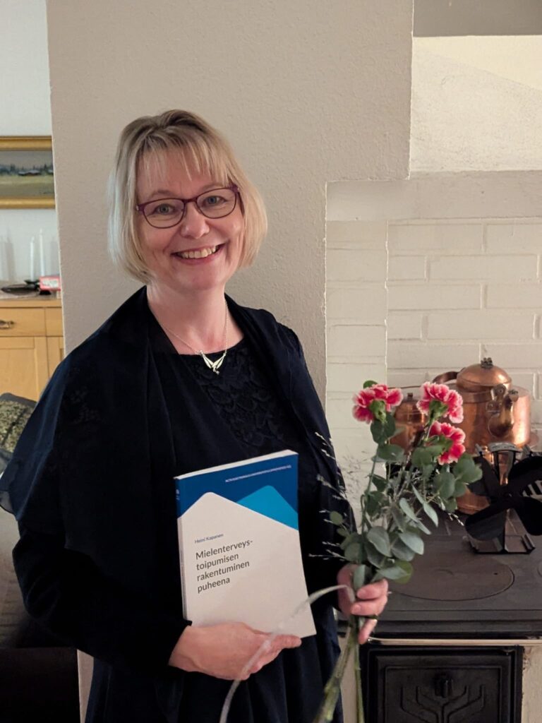 Heini Kapanen hymyilee käsissään kukkakimppu ja oma väitöskirjansa.