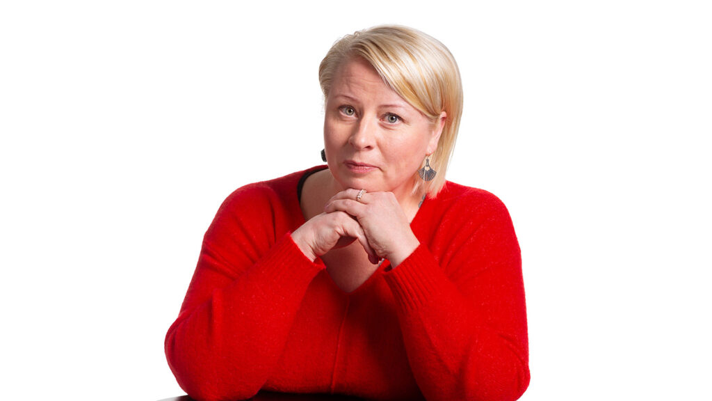 Tuija Nissinen hymyilee. Hänellä on vaalea lyhyt polkkatukka ja punainen neule.