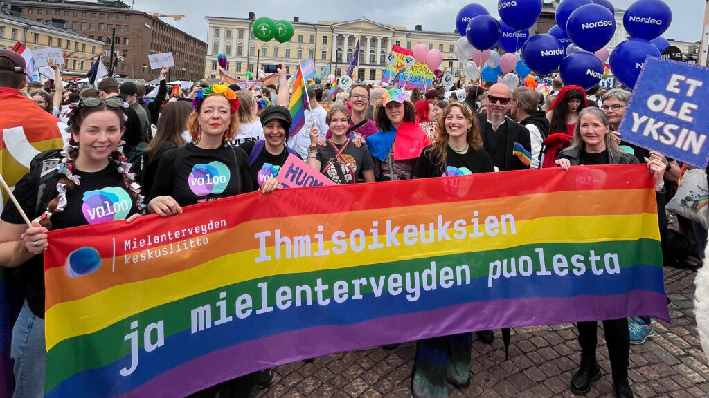 Mielenterveyden työntekijät pitelevät käsissään isoa banderollia, jossa lukee sateenkaaren värien päällä "Ihmisoikeuksien ja mielenterveyden puolesta."