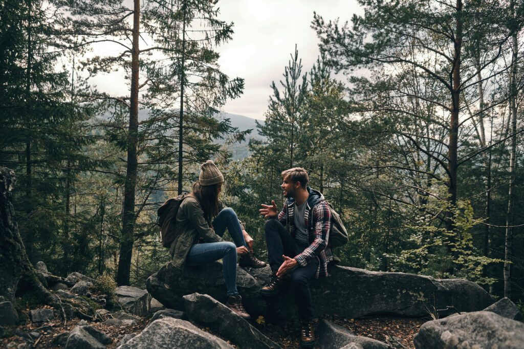 Kaksi retkeilijää istuu kivillä metsässä ja juttelee.